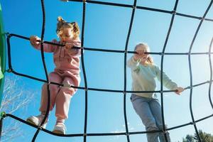 Happy active girls of different ages climbed on a rope web in a playground against a bright blue sky on a sunny day. photo