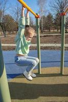 A sports girl of nine years is engaged in a horizontal bar in the park while walking on a sunny day