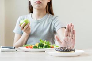 Diet, Dieting asian young woman or girl use hand push out, deny sweet donut and choose green salad vegetables, eat food for good healthy, health when hungry. Close up female weight loss person. photo