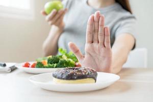 dieta, dieta asiático joven mujer o niña utilizar mano empujar afuera, negar dulce rosquilla y escoger verde ensalada verduras, comer comida para bueno saludable, salud cuando hambriento. cerca arriba hembra peso pérdida persona. foto