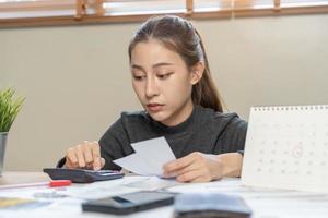 financiero deber asiático mujer, hembra sentado en piso hogar, estresado y confuso por calcular gastos desde factura o factura, tener No dinero a pagar, hipoteca o préstamo. deuda, bancarrota o arruinado concepto. foto