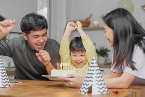 contento cumpleaños fiesta en familia, asiático joven padre padre, madre y pequeño linda chico o niño celebrando, soplo velas en el pastel y decorado globos, celebracion a hogar. encantador momentos foto