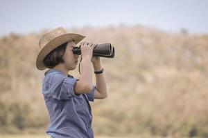 mujer use sombrero y sostenga binocular en el campo de hierba foto