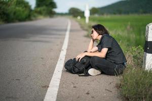 Woman sit with backpack hitchhiking along a road in countryside photo