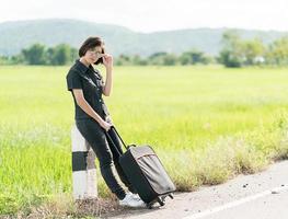 Woman with luggage hitchhiking along a road photo