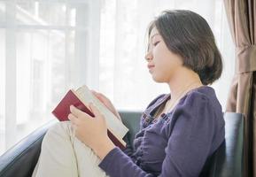 joven mujer asiática de pelo corto lee un libro en la sala de estar foto