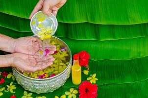 Songkran festival background with hand pouring water and flowers to elder people for blessing with scented water on wet banana leaf background. photo