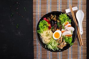 Japanese ramen soup with chicken, egg, shimeji mushrooms and eggplants on dark wooden background. Chanko nabe, sumo soup. Top view photo
