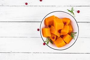 Baked sweet pumpkin with rosemary and cranberries in a bowl on a white wooden background. View from above photo