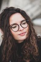 Beautiful young woman with brunette curly hair, portrait in eye glasses enjoying the sun in the city. photo