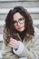 hermosa joven mujer con morena Rizado cabello, retrato en ojo lentes disfrutando el Dom en el ciudad. foto