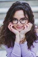 Beautiful young woman with brunette curly hair, portrait in eye glasses enjoying the sun in the city. photo