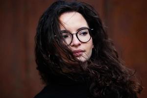 Beautiful young woman with brunette curly hair, portrait in eye glasses enjoying the sun in the city. photo