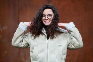 hermosa joven mujer con morena Rizado cabello, retrato en ojo lentes disfrutando el Dom en el ciudad. foto