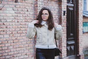 Beautiful young woman with brunette curly hair, portrait in eye glasses enjoying the sun in the city. photo