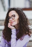 Beautiful young woman with brunette curly hair, portrait in eye glasses enjoying the sun in the city. photo