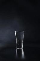 cerca arriba de vaso de vodka en un negro antecedentes. bebida transparente vaso en un negro antecedentes. aislar. Copiar espacio foto