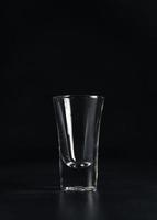 vertical Disparo de vacío vaso de vodka en negro antecedentes. un vacío bebida transparente vaso en un negro antecedentes. aislar. Copiar espacio