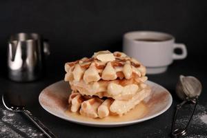 Homemade of tasty Belgian Waffles Plate, Caramel Sauce, Coffee Cup, Milk on a Black concrete Background photo