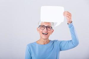 retrato de un un emocionado maduro gris pelo mujer demostración blanco habla burbuja aislado terminado gris antecedentes. mayor mujer participación habla burbuja bandera foto