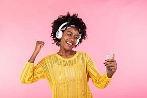 Gadgets are future. Portrait of excited happy African American woman with afro hairstyle wearing trendy top and headphones dancing while listening music on her smartphone