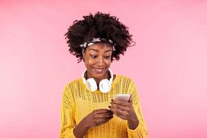 African american woman wearing headphones and smiling. Young woman with natural curly hair holding and looking at mobile phone.