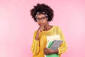 Beautiful young african american woman holding notebooks, wearing glasses. Having thinking face. Student life photo