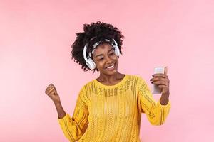 Lifestyle Concept - Portrait of beautiful African American woman joyful listening to music on mobile phone. trendy stylish cute girl in headphones listening to music dancing isolated pink background