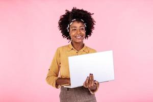 African american woman holding laptop smiling and looking at camera. Young beautiful woman feeling happy, standing isolated over pink background photo
