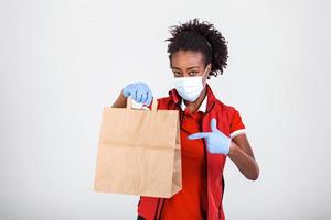 Delivery woman employee in red t-shirt uniform mask glove hold craft paper packet with food isolated on white background studio Service quarantine pandemic coronavirus virus 2019-ncov concept photo