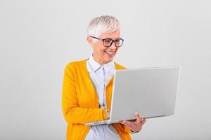 Image of cheerful mature woman standing isolated over gray background using laptop computer. Portrait of a smiling senior lady holding laptop computer photo