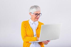 imagen de alegre maduro mujer en pie aislado terminado gris antecedentes utilizando ordenador portátil computadora. retrato de un sonriente mayor dama participación ordenador portátil computadora foto