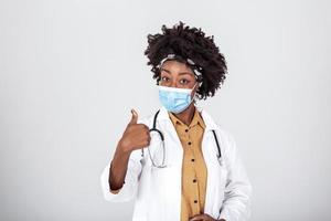 African american female doctor wear white medical coat stethoscope face mask showing thumb up. Brave proud black hero physician on grey, healthcare safety, medicine protection photo