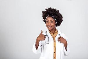 Happy african female doctor wear white lab coat, stethoscope look at camera and showing thumbs up. Smiling afro american woman professional therapist physician portrait. photo