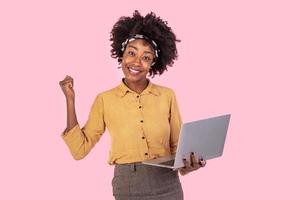 Happy excited african american woman holding laptop and raising her arm up to celebrate success or achievement.Young beautiful woman feeling happy because of business success photo