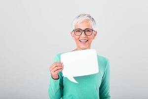 Happy mature woman in plain blue long sleeve t-shirt holding empty speech bubble isolated on background. Woman showing sign speech bubble banner looking happy photo