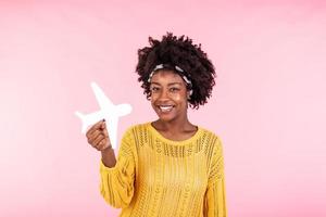 Photo of African American positive cute pretty beautiful girl won tickets to go abroad by air plane rejoicing excited emotions holding plane isolated curly wavy pink vivid color background