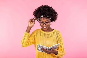 Attractive african american woman holding notebook and pen. Young woman with glasses holding open textbook and smiling while thinking. Education concept photo