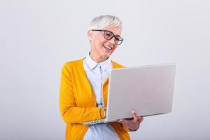 imagen de alegre maduro mujer en pie aislado terminado gris antecedentes utilizando ordenador portátil computadora. retrato de un sonriente mayor dama participación ordenador portátil computadora foto