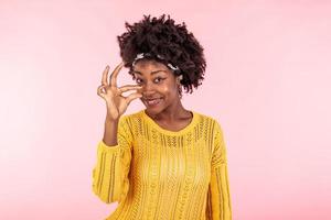 Positive cheerful dark skinned curly woman shapes something very little with fingers, demonstrates small decreased price or salary, gestures not big object, smiles toothily photo