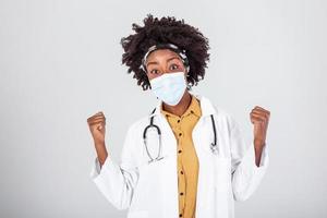 Happy satisfied female African American doctor wearing protective face mask and safety goggles,eyes smiling,studio portrait isolated ,content relief after end of global COVID-19 pandemic crisis photo