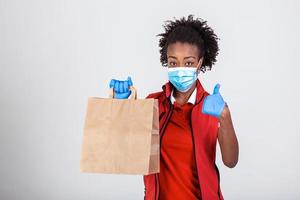 Delivery woman employee in red t-shirt uniform mask glove hold craft paper packet with food isolated on white background studio Service quarantine pandemic coronavirus virus 2019-ncov concept photo