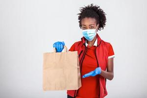 Delivery woman employee in red t-shirt uniform mask glove hold craft paper bag with food isolated on white background studio Service quarantine pandemic coronavirus virus 2019-ncov concept photo