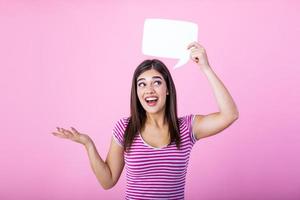 Young beautiful girl holding a bubble for text, isolated on a pink background. Young woman with smile holding blank speech bubble against background photo