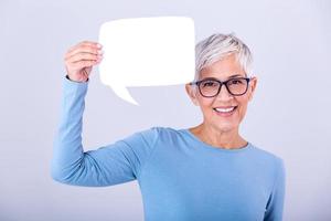 Happy mature woman in plain blue long sleeve t-shirt holding empty speech bubble isolated on background. Woman showing sign speech bubble banner looking happy photo