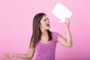 cute woman screaming in blank speech bubble isolated background. Young woman holding a speech bubble on a pink background photo
