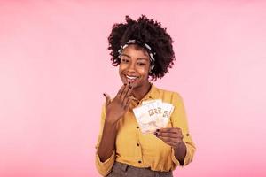 Portrait of a cheerful young woman holding money. African american woman holding euro bank notes, feeling happy and satisfied photo