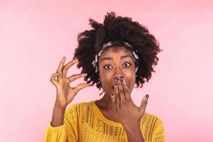 Size matters. Pleased African American young woman demonstrates very tiny object, smiles positively, wears casual sweater, poses against pink background, shapes small thing. Body language concept photo