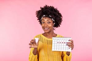 Young African American woman holding periods calendar for checking menstruation days and menstrual cup, feminine hygiene alternative product instead of tampon during period. photo