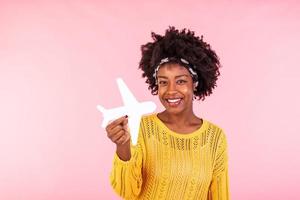 Photo of African American positive cute pretty beautiful girl won tickets to go abroad by air plane rejoicing excited emotions holding plane isolated curly wavy pink vivid color background